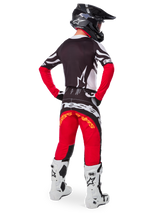 Motocross-Fahrer von hinten im Alpinestars Limited Edition Techstar Deep Trikot in Black White High Red, mit schwarzer Rückseite, weißem Stern-Logo und roten Ärmeln, kombiniert mit einer passenden rot-schwarzen Hose, weiß-schwarzen Stiefeln und einem schwarzen Helm für eine komplette Offroad-Rennausrüstung.