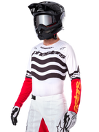 Motocross-Fahrer im Alpinestars Limited Edition Techstar Deep Jersey, weißes Trikot mit schwarzen Wellenstreifen und roten Unterärmeln, kombiniert mit schwarzem Helm, verspiegelter Brille, weiß-schwarzen Handschuhen und weißer Rennsport-Hose, Performance-Motocross-Outfit.