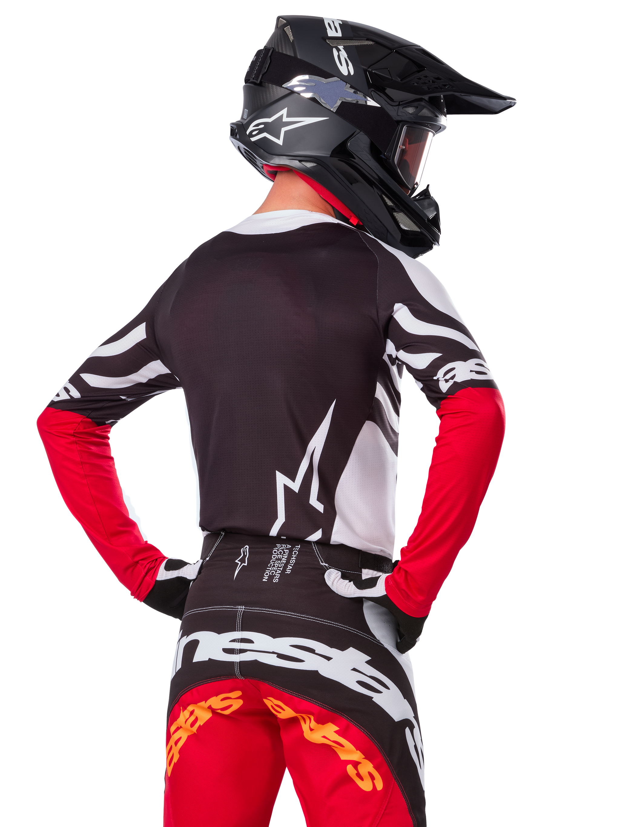 Motocross-Fahrer von hinten mit dem Alpinestars Limited Edition Techstar Deep Jersey in Schwarz, Weiß und High Red, dazu die passende Rennhose und ein schwarzer Helm, athletische Passform für Offroad-Performance
