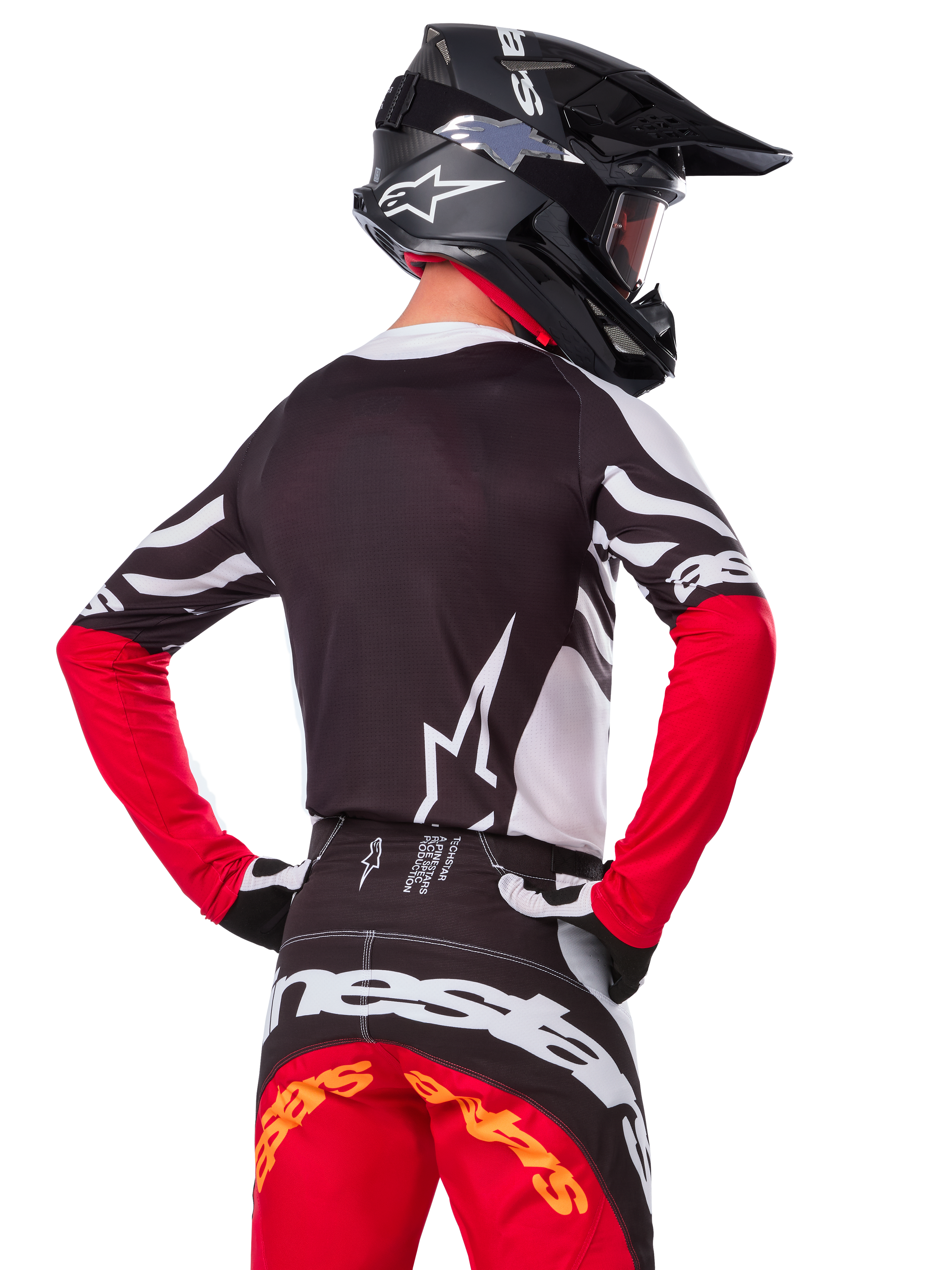 Motocross-Fahrer in kompletter Rennausrüstung, Alpinestars Limited Edition Techstar Deep Jersey in Schwarz, Weiß und High Red, Rückansicht, passende Techstar Deep Hose, schwarzer Helm mit Brille, schwarz-weiße Handschuhe, professionelles Offroad-Rennoutfit