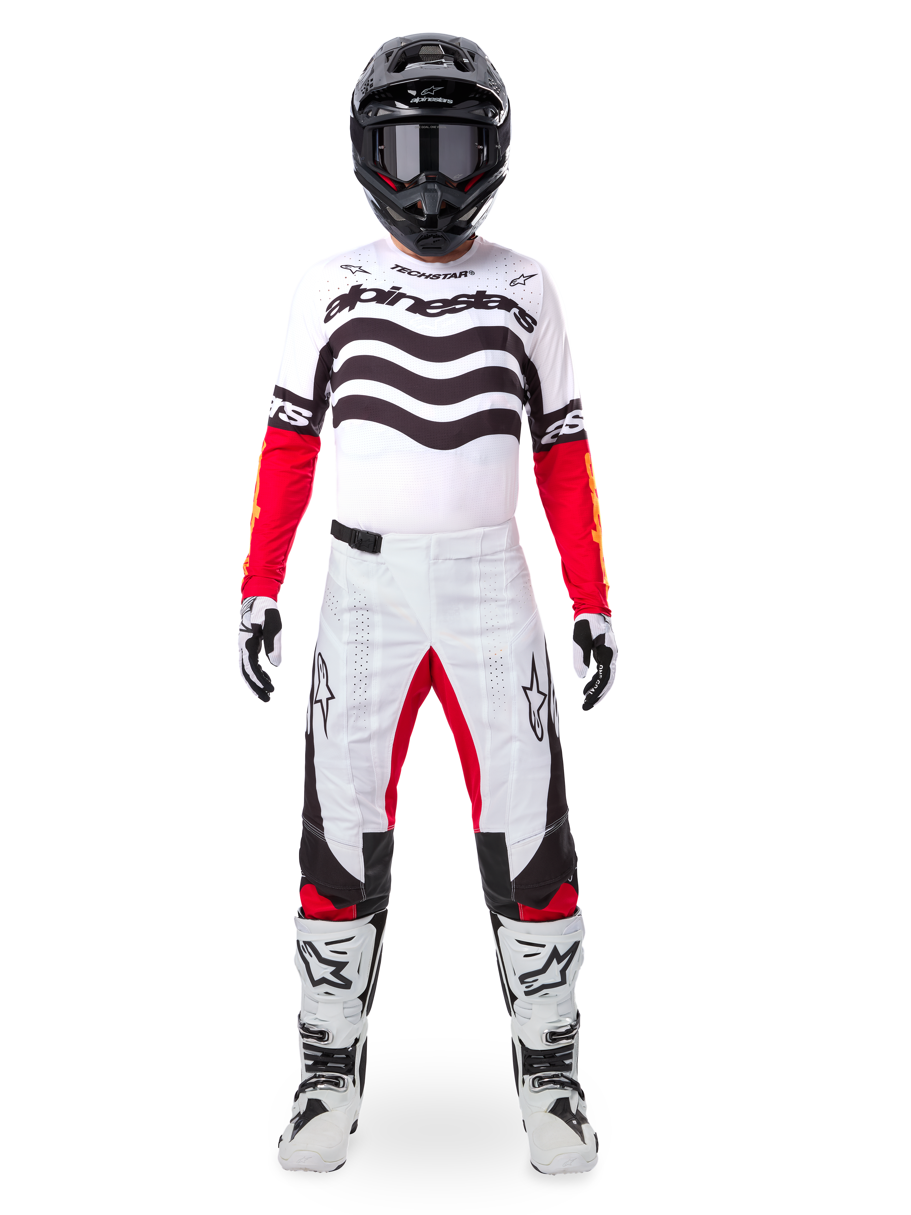 Motocross-Fahrer in der Alpinestars Limited Edition Techstar Deep Ausrüstung, weißes Jersey mit schwarzen Wellengrafiken und roten Ärmeln, passende weiß-schwarze Hose mit roten Akzenten, schwarzer Helm mit dunkler Brille und weiße Stiefel, professionelles Offroad-Outfit