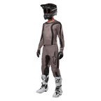 Motocross-Fahrer in kompletter Rennausrüstung mit dem Alpinestars 2024 Fluid Lurv Jersey in Mud Black, kombiniert mit der passenden Hose, schwarzem Helm mit Brille, weiß-schwarzen Stiefeln und schwarzen Handschuhen, koordiniertes Outfit für den Offroad-Rennsport