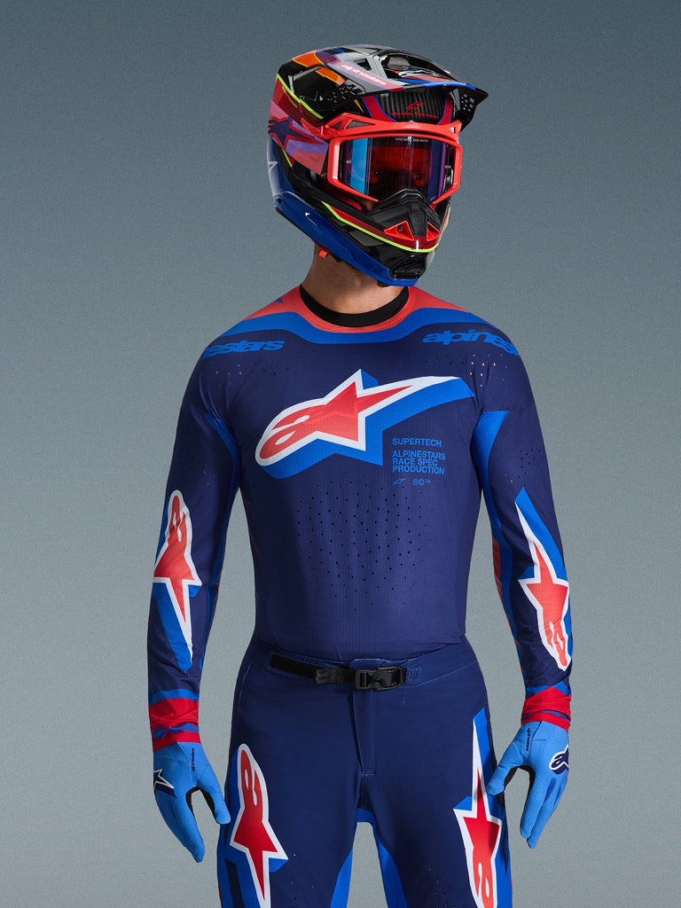 Alpinestars 2026 Supertech Vista Jersey, Motocross Jersey, Dark Navy Hot Coral and Cobalt, worn with matching motocross pants and helmet, featuring large star logo on chest and race spec branding, athletic fit with ventilated mesh panels for elite racing performance
