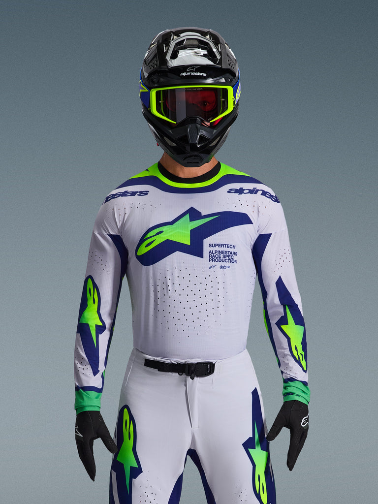 Alpinestars 2026 Supertech Vista Trikot, Motocross-Trikot, Hellgrau, Neongelb und Blau, getragen von einem Fahrer mit passender Hose und schwarzem Helm, mit großem Brustlogo und lasergeschnittenen Perforationen zur Belüftung, athletische Pro-Level-Passform
