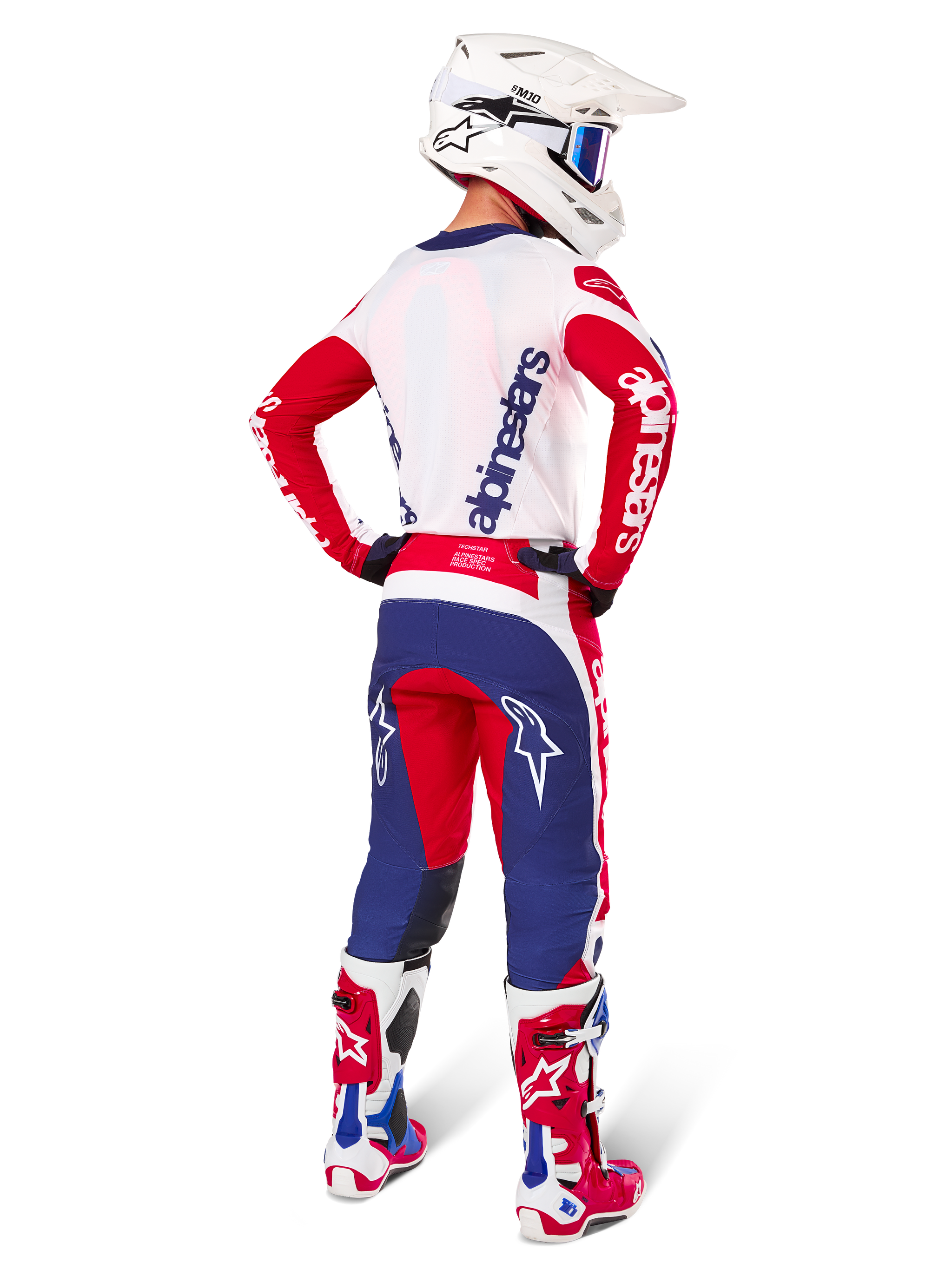 Motocross-Fahrer in der Rückansicht, Alpinestars Limited Edition Techstar Fortitude Jersey in leuchtendem Rot, Weiß und Blau, passende technische Hose mit Stern-Logos, weißer Helm mit Schutzbrille und rot-weiße Stiefel, komplette koordinierte Ausrüstung für Offroad-Rennen
