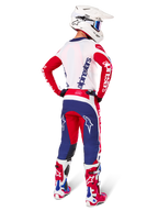 Motocross-Fahrer in der Rückansicht, trägt das Alpinestars Limited Edition Techstar Fortitude Trikot und Ausrüstungsset in der Farbkombination Bright Red White Blue, mit weißem Alpinestars-Branding auf den roten Ärmeln und einem marineblauen Logo auf dem weißen Rücken, kombiniert mit einem weißen Motocross-Helm und passenden Rennstiefeln.