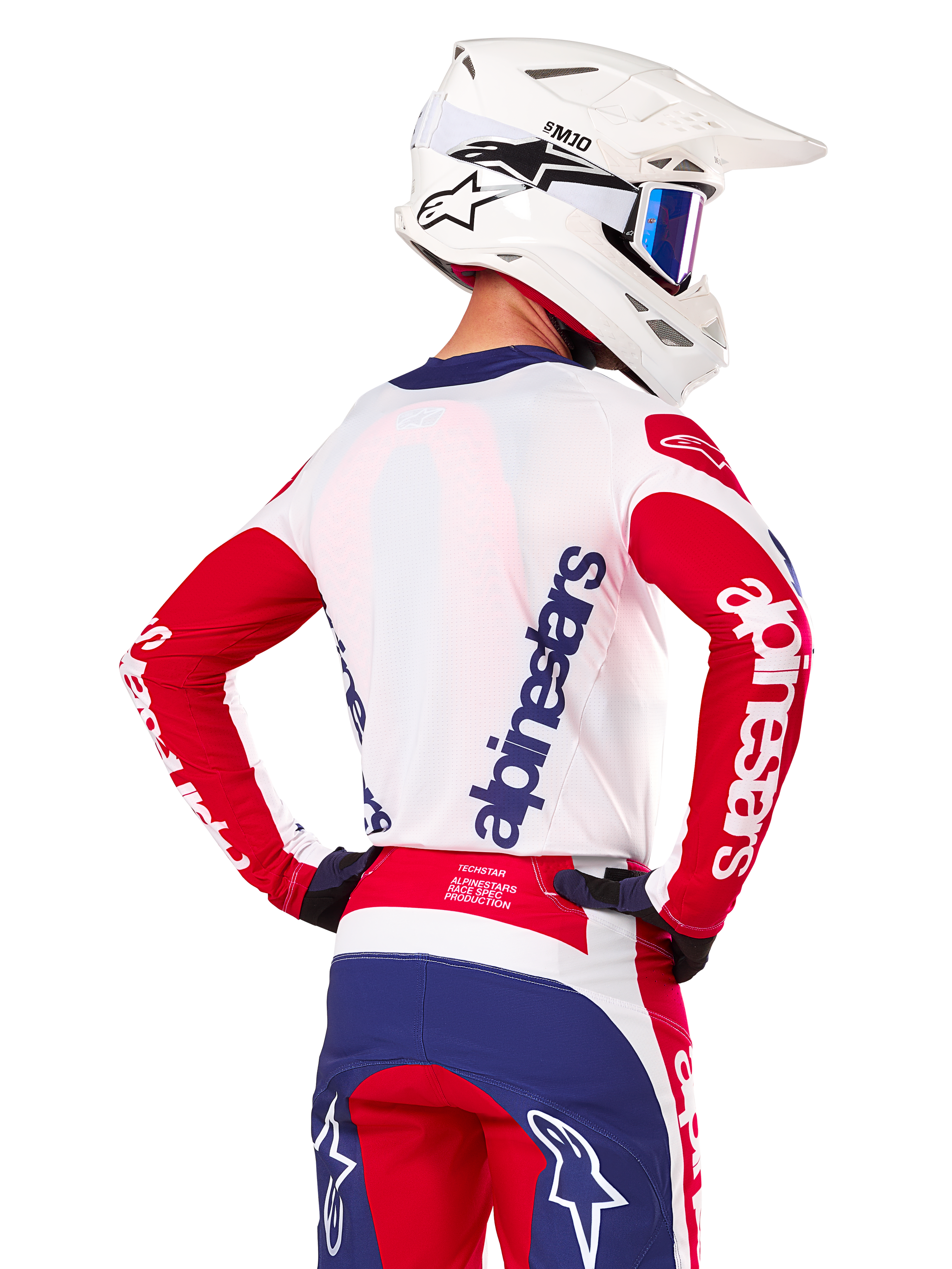 Alpinestars Limited Edition Techstar Fortitude Jersey, Motocross-Trikot, Hellrot, Weiß und Blau, Rückansicht eines Fahrers mit weißem Helm und passender Ausrüstung, markante Alpinestars-Logos auf dem Rücken und den Ärmeln, entwickelt für Hochleistungs-Offroad-Rennsport