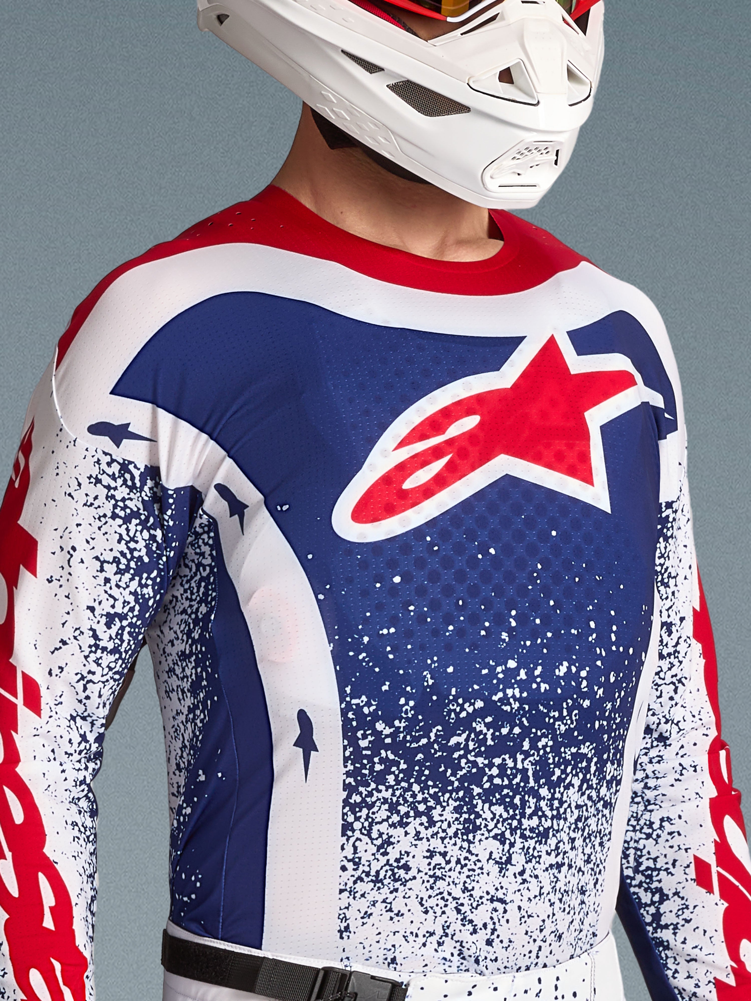 Alpinestars Techstar Unity Trikot Limited Edition, blau-weißes Motocross-Trikot für Herren mit rotem Stern-Logo und weißem Helm.