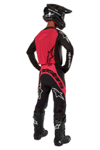 Motocross-Fahrer von hinten im 2024 Supertech Ward Jersey in Black Red Berry, mit leuchtend roter Rückenpartie und schwarzen Ärmeln mit weißem Alpinestars-Logo, kombiniert mit passender Motocross-Hose, schwarzen Tech 10 Stiefeln und einem schwarzen Carbonhelm, professionelles Rennsport-Ausrüstungsset.