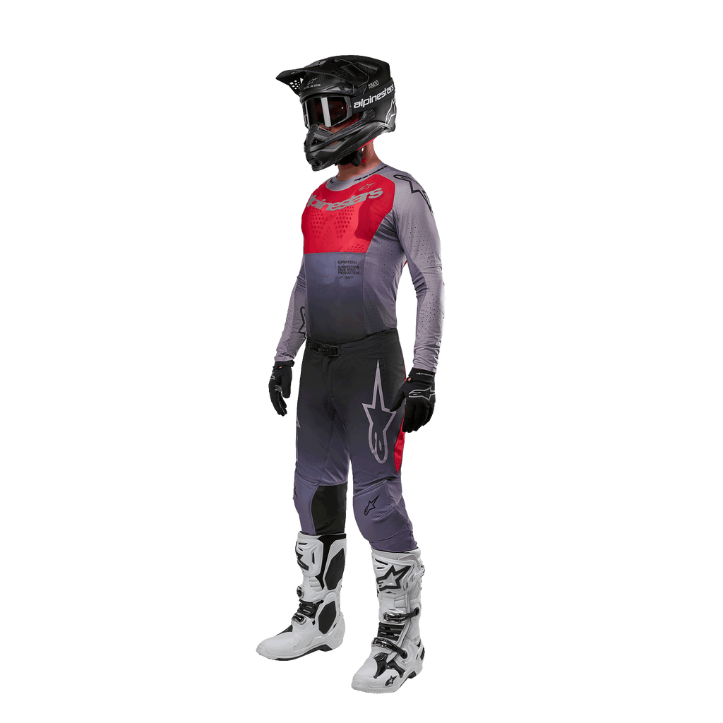 Motocross-Fahrer in kompletter Rennausrüstung, Alpinestars 2024 Supertech Dade Trikot in Iron Red Berry und Grau, passende graue Hose mit roten Akzenten, schwarzer Helm mit Goggles, weiß-schwarze Stiefel, schwarze Handschuhe, abgestimmtes Outfit für den Offroad-Rennsport