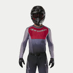Motocross-Fahrer im Alpinestars 2024 Supertech Dade Jersey in Iron Red Berry, mit rotem Brustbereich und grauen Ärmeln mit silbernem Branding, getragen mit passender Hose, einem schwarzen Helm und schwarzen Handschuhen, professionelle Offroad-Rennausrüstung