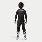 Motocross-Fahrer in kompletter Rennausrüstung, Alpinestars 2024 Fluid Graphite Trikot in Schwarz-Silber, schwarze Hose mit silbernen Stern-Logos, schwarzer Helm mit roter Brille, weiß-schwarze Stiefel, weiß-schwarze Handschuhe, abgestimmtes Motocross-Outfit