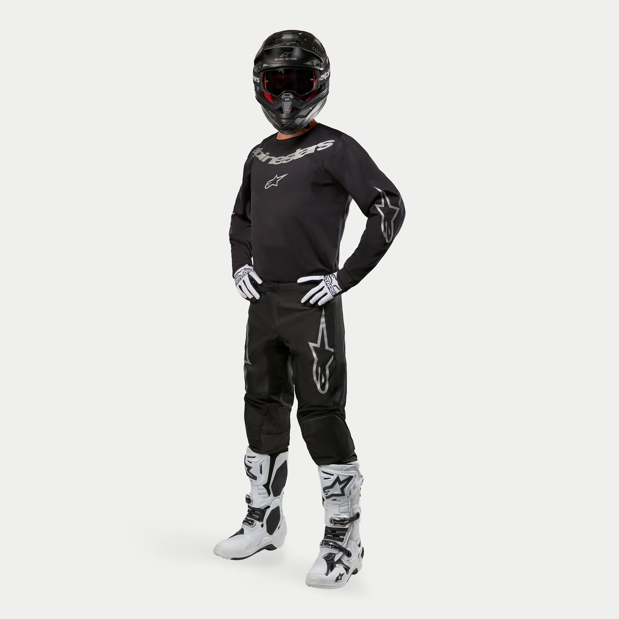 Motocross-Fahrer mit Alpinestars 2024 Fluid Graphite Trikot in Schwarz und Silber, passender schwarzer Hose mit silbernen Stern-Logos, weiß-schwarzen Stiefeln, weiß-schwarzen Handschuhen und einem schwarzen Helm mit roter Brille, komplette Offroad-Rennausrüstung
