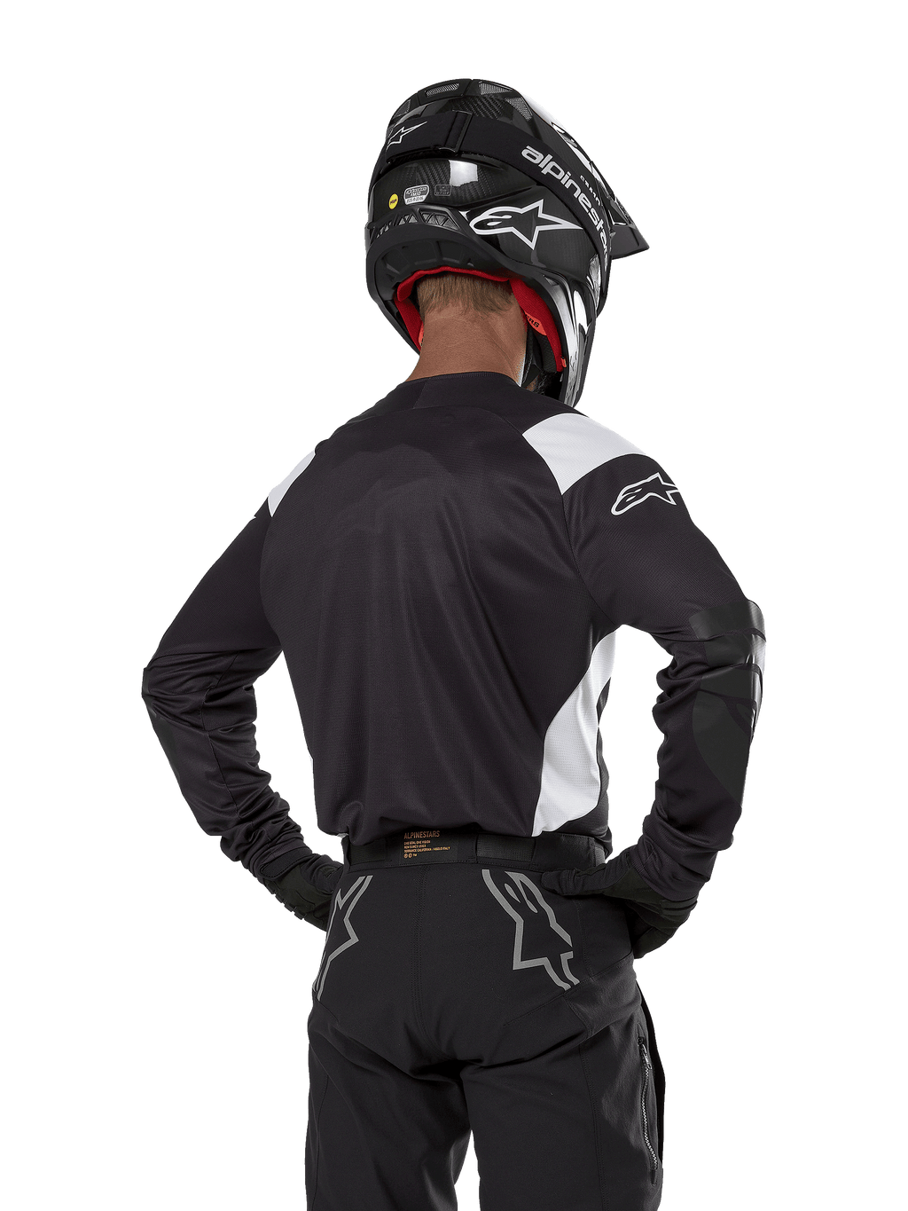 Alpinestars Techdura Trikot, Schwarz mit weißen Schulterakzenten, Rückansicht eines Motocross-Fahrers mit passender schwarzer Hose und Helm, verstärkte Ellbogen-Patches, Enduro- und Offroad-Rennausrüstung