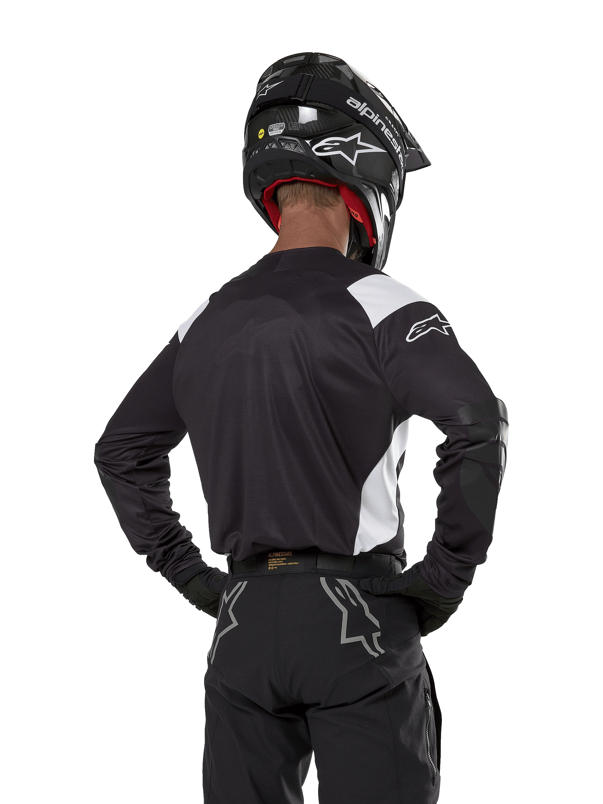 Alpinestars Techdura Trikot, Schwarz mit weißen Schulterakzenten, Rückansicht eines Motocross-Fahrers mit passender schwarzer Hose und Helm, verstärkte Ellbogen-Patches, Enduro- und Offroad-Rennausrüstung