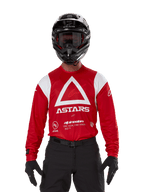 Motocross-Fahrer im Alpinestars Techdura Jersey, Hellrot mit weißen Grafiken, großes weißes Dreieck und ASTARS-Logo auf der Brust, kombiniert mit schwarzem Helm, schwarzer Brille und schwarzer Rennausrüstung, abgestimmtes Outfit für Enduro- und Offroad-Rennen