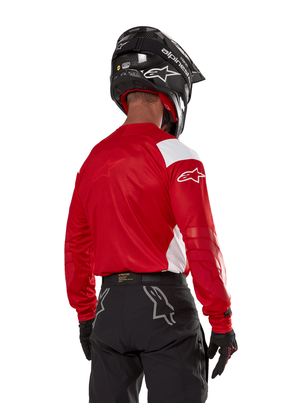 Motocross-Fahrer in der Rückansicht, trägt das Alpinestars Techdura Jersey in Bright Red mit weißen Einsätzen, kombiniert mit einer schwarzen Offroad-Hose, einem schwarzen Helm und schwarzen Handschuhen, abgestimmte Ausrüstung für Enduro- und Motocross-Sport
