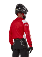 Motocross-Fahrer in der Rückansicht, trägt das Alpinestars Techdura Jersey in Bright Red mit weißen Einsätzen, kombiniert mit einer schwarzen Offroad-Hose, einem schwarzen Helm und schwarzen Handschuhen, abgestimmte Ausrüstung für Enduro- und Motocross-Sport