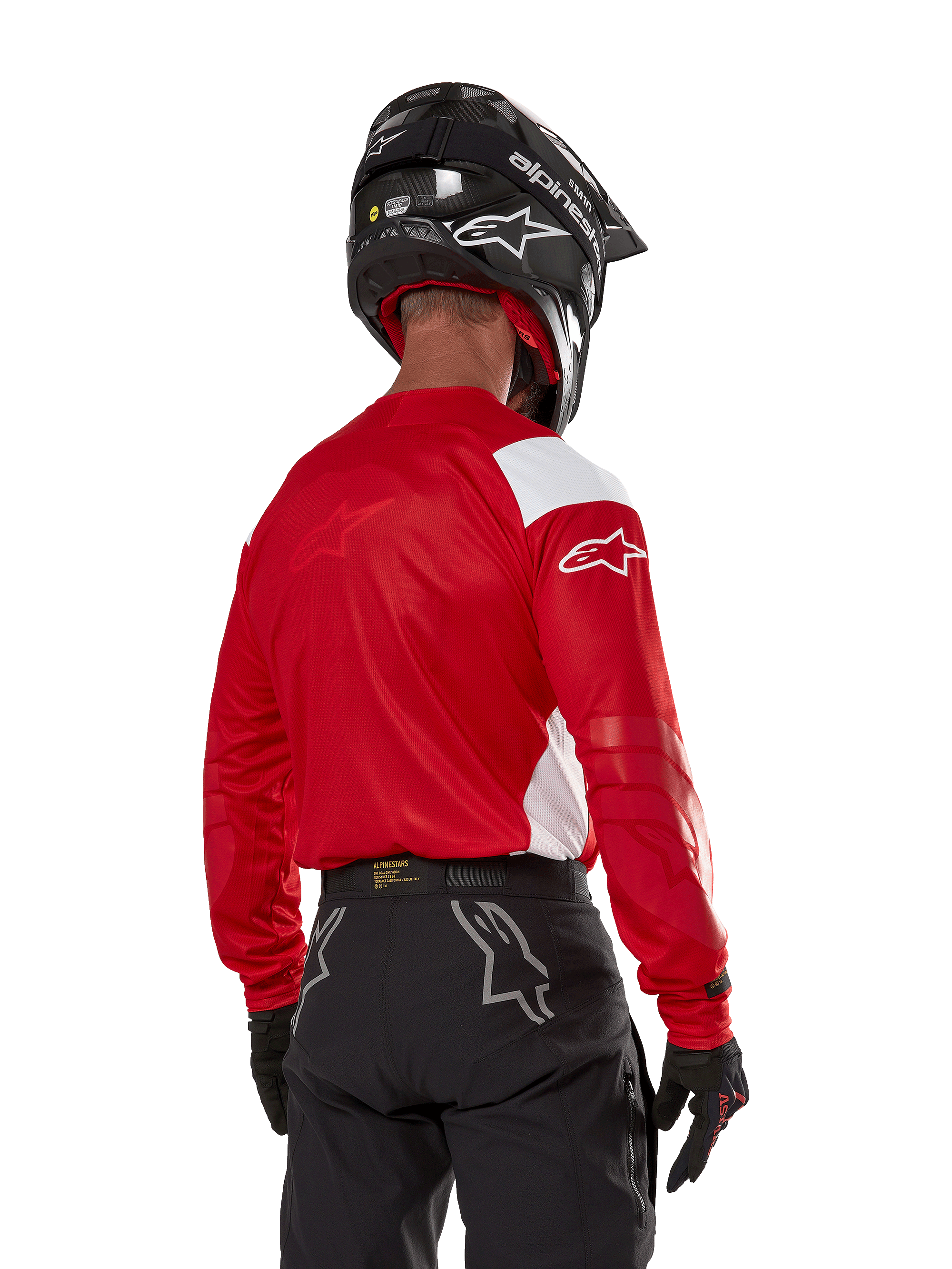Motocross-Fahrer in der Rückansicht, trägt das Alpinestars Techdura Jersey in Bright Red mit weißen Einsätzen, kombiniert mit einer schwarzen Offroad-Hose, einem schwarzen Helm und schwarzen Handschuhen, abgestimmte Ausrüstung für Enduro- und Motocross-Sport