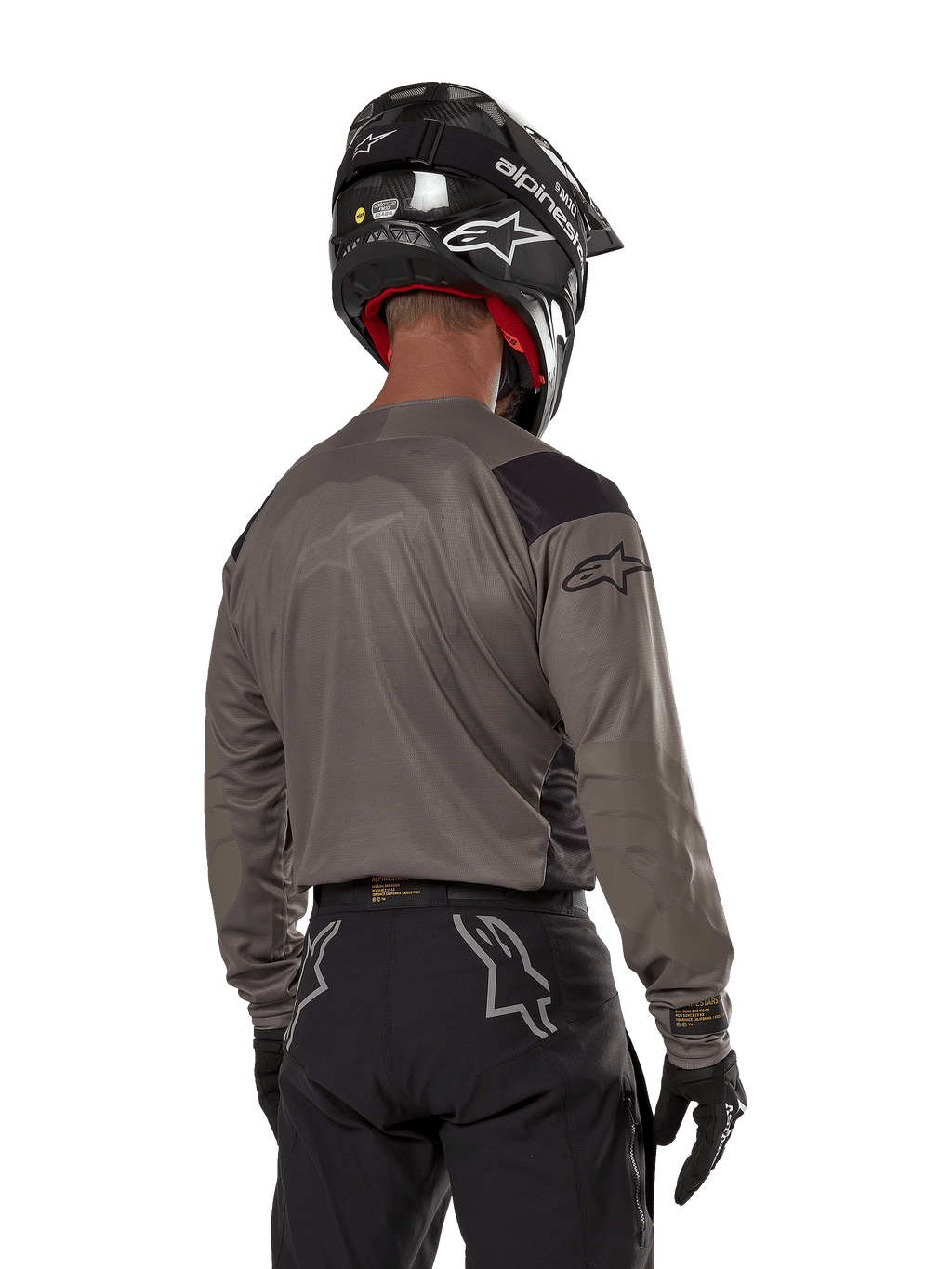 Motocross-Fahrer von hinten im Alpinestars Techdura Jersey in Falcon Brown, kombiniert mit einer schwarzen Offroad-Hose und einem schwarzen Helm, modernes Grafikdesign und verlängerte Rückseite für Enduro-Fahrten