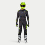 Motocross-Fahrer in kompletter Rennausrüstung, 2024 Techstar Rantera Jersey in Schwarz, Navy und Gelb Fluo, passende Hose mit abstraktem Muster, leuchtend fluo-gelber Helm, weiß-schwarze Stiefel, abgestimmtes Outfit für den Offroad-Rennsport