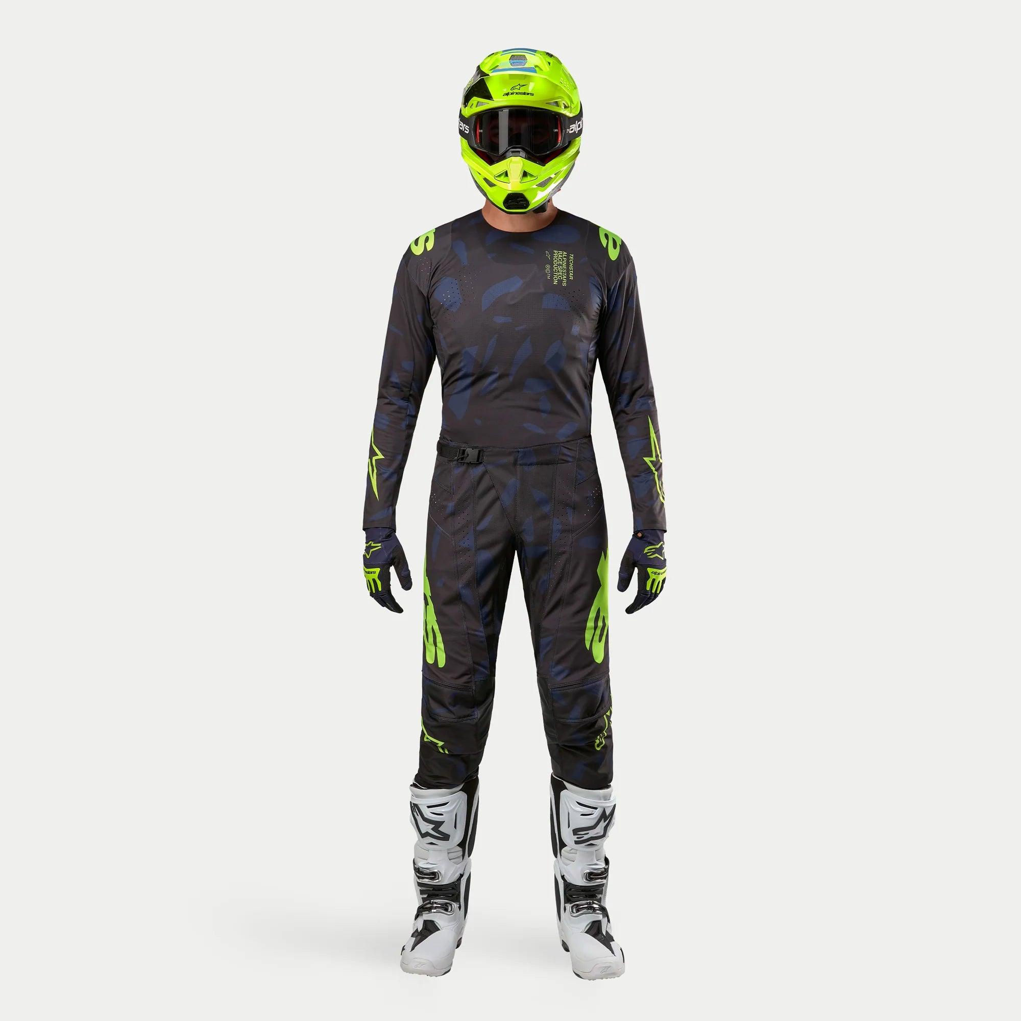 Motocross-Fahrer in kompletter Rennausrüstung, 2024 Techstar Rantera Jersey in Schwarz, Navy und Gelb Fluo, passende Hose mit abstraktem Muster, leuchtend fluo-gelber Helm, weiß-schwarze Stiefel, abgestimmtes Outfit für den Offroad-Rennsport