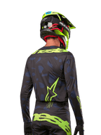Rückansicht eines Motocross-Fahrers im Alpinestars 2024 Techstar Rantera Jersey in Schwarz Navy Gelb Fluo, mit auffälligem neongelbem Branding und Logos auf dem Rücken, kombiniert mit der passenden Motocross-Hose und einem neongelben Helm für einen kompletten Offroad-Racing-Look.