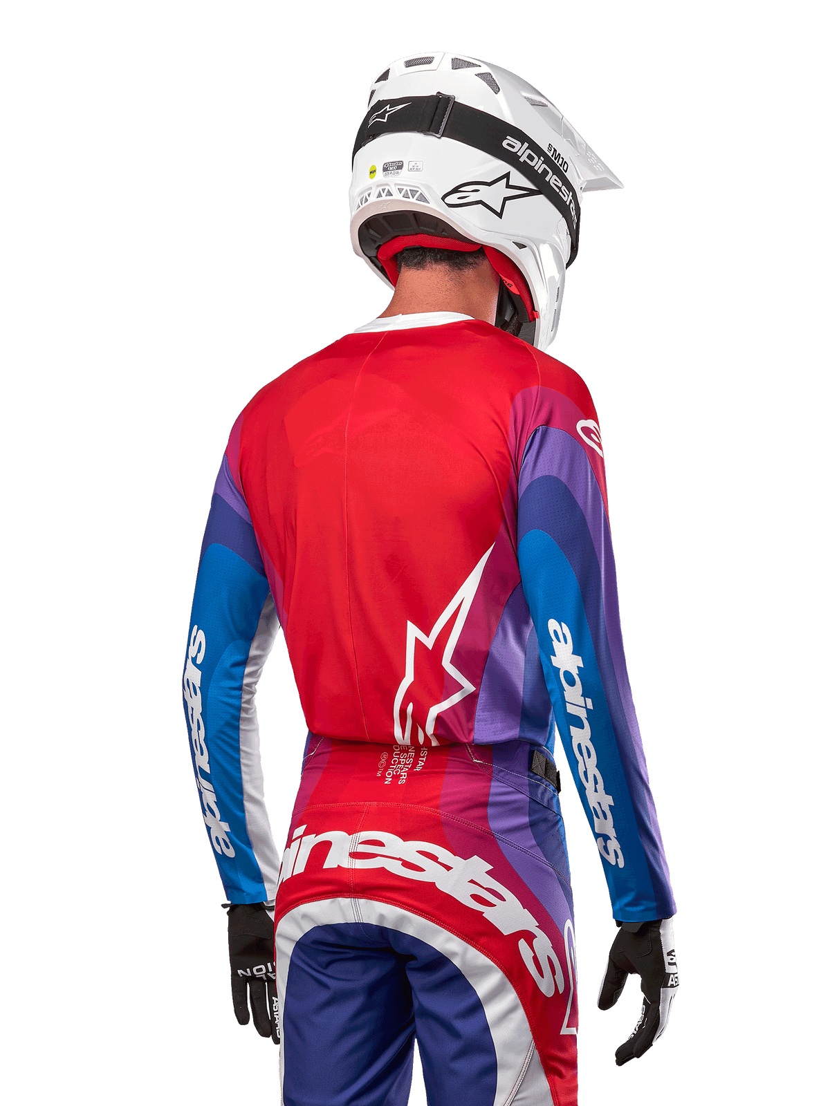 Motocross-Fahrer von hinten im Alpinestars 2024 Techstar Pneuma Jersey in Blue Mars Red White, mit einer roten Rückseite und weißem Stern-Logo, blau-violetten Ärmeln mit weißem Branding, kombiniert mit passender Hose und einem weißen Helm für den Offroad-Rennsport.