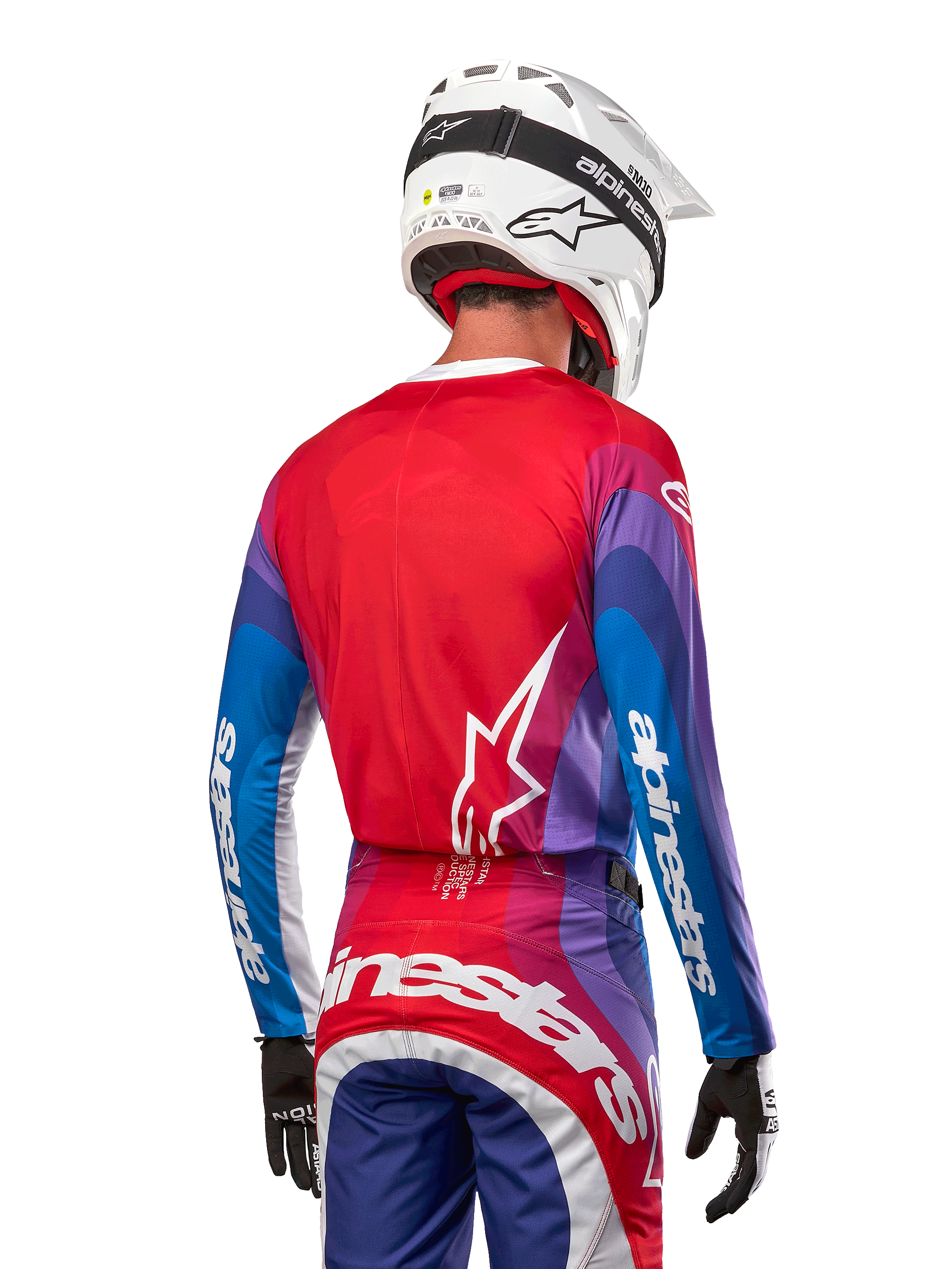 Motocross-Fahrer von hinten im Alpinestars 2024 Techstar Pneuma Jersey in Blue Mars Red White, mit einer roten Rückseite und weißem Stern-Logo, blau-violetten Ärmeln mit weißem Branding, kombiniert mit passender Hose und einem weißen Helm für den Offroad-Rennsport.