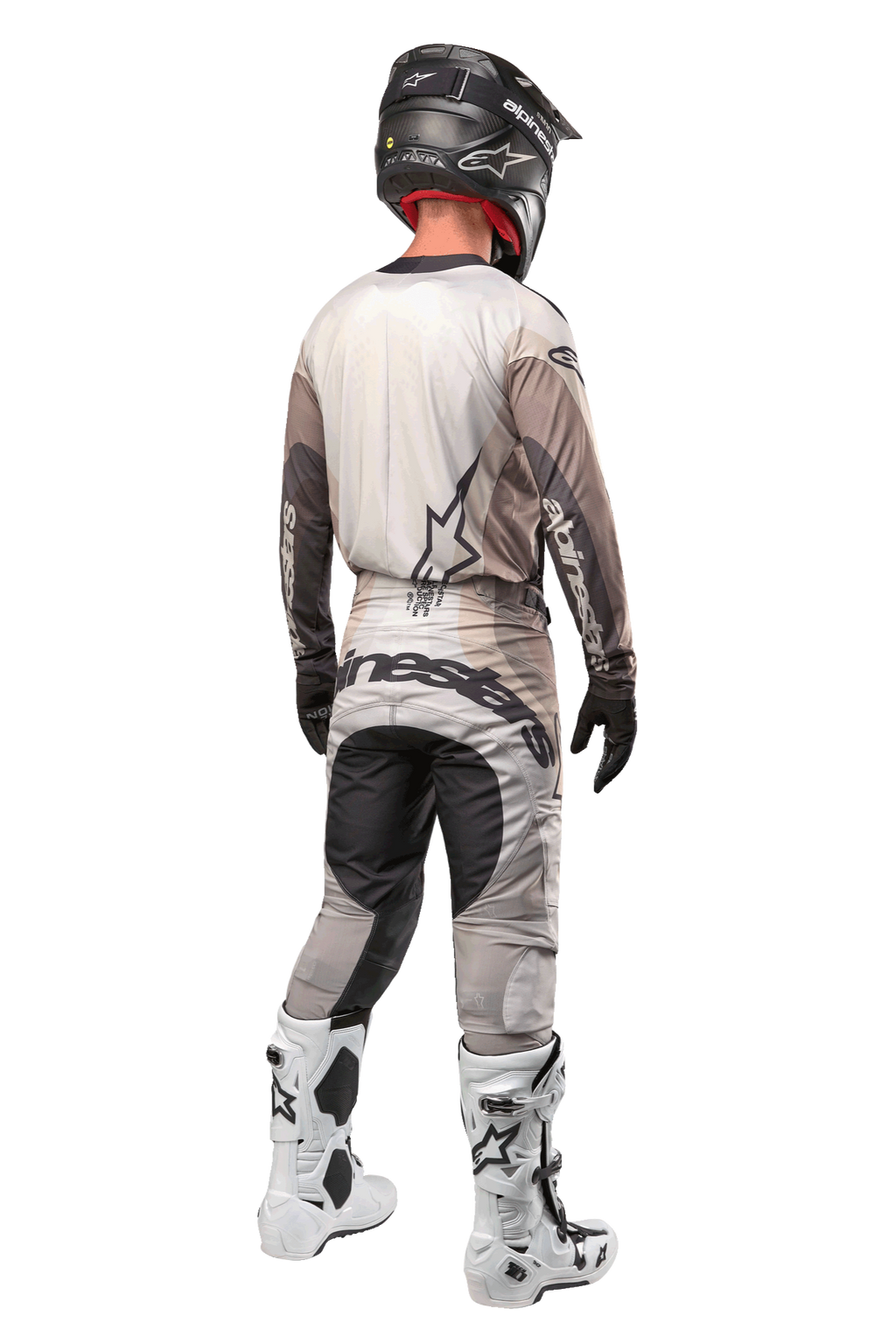 Motocross-Fahrer in der Rückansicht im 2024 Techstar Pneuma Trikot in Dark Sand Iron Dust Gray, passende Motocross-Hose mit markantem Branding, schwarzer Helm und weiße Rennstiefel, abgestimmte professionelle Offroad-Ausrüstung.