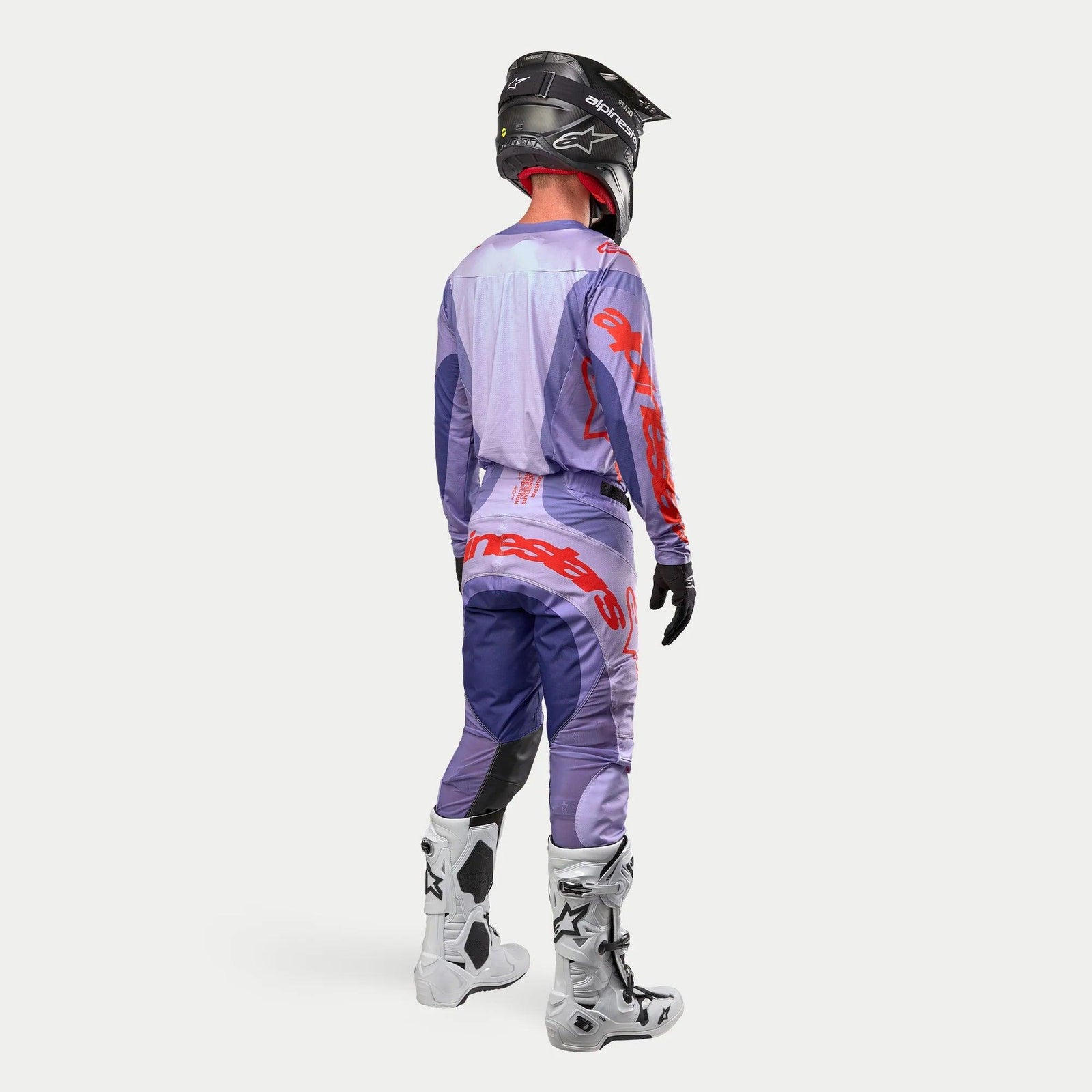 Alpinestars 2024 Techstar Ocuri Ausrüstung, Motocross-Komplettset mit Trikot und Hose in Lila und Hot Orange, schwarzer Helm, weiße Motocross-Stiefel, schwarze Handschuhe, Rückansicht der sportlichen Rennausrüstung