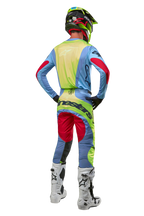 Motocross-Fahrer von hinten im Alpinestars 2024 Techstar Ocuri Jersey, Hellblau mit Akzenten in Gelb Fluo und Red Berry, passender Rennhose, weißen Stiefeln und Neon-Helm, komplette Offroad-Ausrüstung für den professionellen Wettbewerb