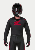 Motocross-Fahrer im Alpinestars Honda Racer Iconic Trikot in Schwarz und Rot, mit einem großen roten Honda-Flügel-Logo auf der Brust und weißem Astar-Logo, kombiniert mit einem passenden schwarzen Helm, einer Brille und Handschuhen für eine komplette Offroad-Rennausrüstung