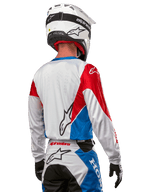 Motocross-Fahrer im Alpinestars Honda Racer Iconic Trikot, Rückansicht, Weiß mit leuchtend blauen und leuchtend roten Paneelen, markantes Alpinestars-Logo auf der Rückseite, kombiniert mit weißem Motocross-Helm und passender Rennhose.