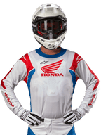 Honda Racer Iconic Trikot, weißes Motocross-Trikot mit rotem Honda-Logo und leuchtend blauen und roten Akzenten, getragen von einem Fahrer mit weißem Helm und Handschuhen, Performance-Ausrüstung für Offroad- und Motocross-Rennsport