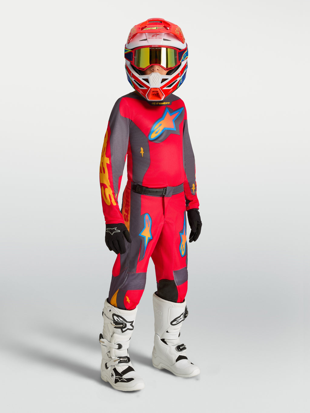 Alpinestars Fluid Hunt Jugend-Trikot und Gear Set, Jugend-Motocross-Outfit in Rot und Grau mit weißen Motorradstiefeln.