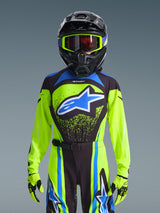 Alpinestars 2026 Jugend Supertech Nomur Jersey, Neongelb mit dunkelblauen und blauen Akzenten, getragen von einem Fahrer mit schwarzem Motocross-Helm, neongelber Brille und passenden Handschuhen, markantes blaues Stern-Logo auf der Brust, Pro-Level Offroad-Rennausrüstung