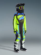 Jugend-Motocross-Fahrer in kompletter Rennausrüstung, 2026 Youth Supertech Nomur Jersey in Gelb Fluo und Dunkelblau, passende Hose mit blauen Akzenten, schwarzer Helm mit neongelber Brille, weiß-schwarze Stiefel, koordiniertes Outfit für den Offroad-Rennsport