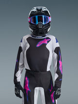 Young motocross rider wearing the Alpinestars 2026 Youth Fluid Grid Jersey in Black, Light Gray, and Purple, paired with matching grid-patterned pants, black helmet with blue-lensed goggles, and black gloves, complete gear set for youth off-road racing.