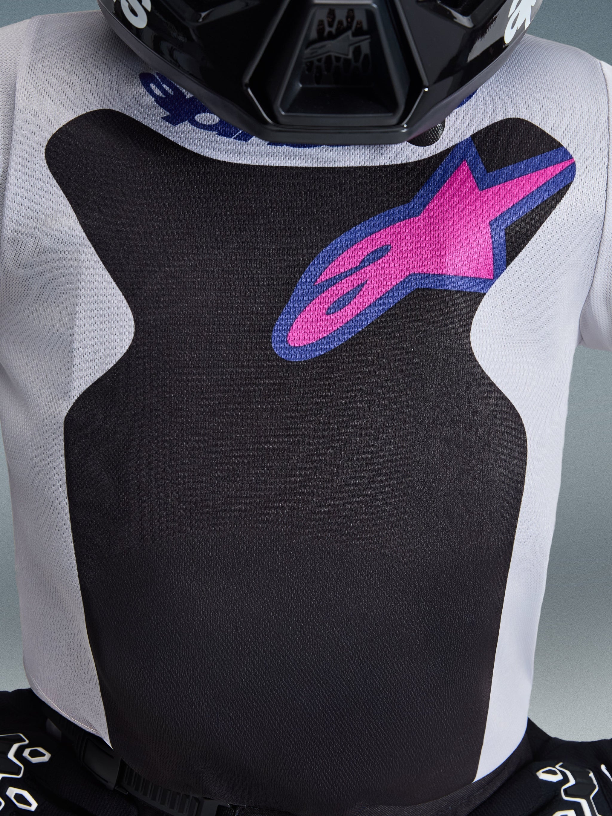 Alpinestars 2026 Youth Fluid Grid Jersey, Motocross Jersey, Black and Light Gray, featuring a pink Alpinestars logo with a blue border on the chest, close-up showing the moisture-wicking fabric texture, part of a coordinated youth racing outfit
