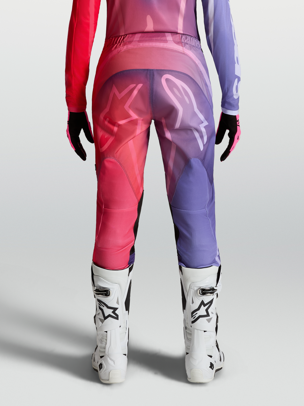 Alpinestars Stella Fluid Kepler Hose, Damen-Motocross-Hose in Lila und Rot, Rückansicht mit ergonomischem Schnitt, 600D-Polygewebe und weißen Logo-Grafiken, getragen mit weißen MX-Stiefeln.
