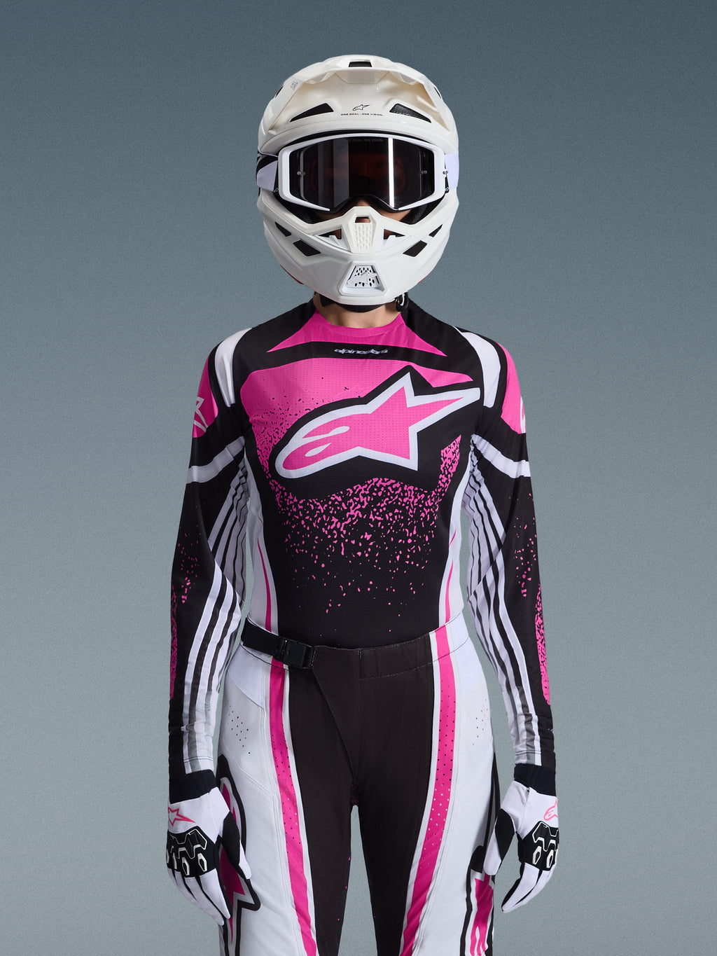 Alpinestars 2026 Stella Techstar Nomur Gear Set, Damen-Motocross-Outfit, Pink, Schwarz und Weiß mit großem Stern-Logo, passendes Jersey, Hose und Handschuhe mit einem weißen Helm, Vorderansicht auf grauem Hintergrund