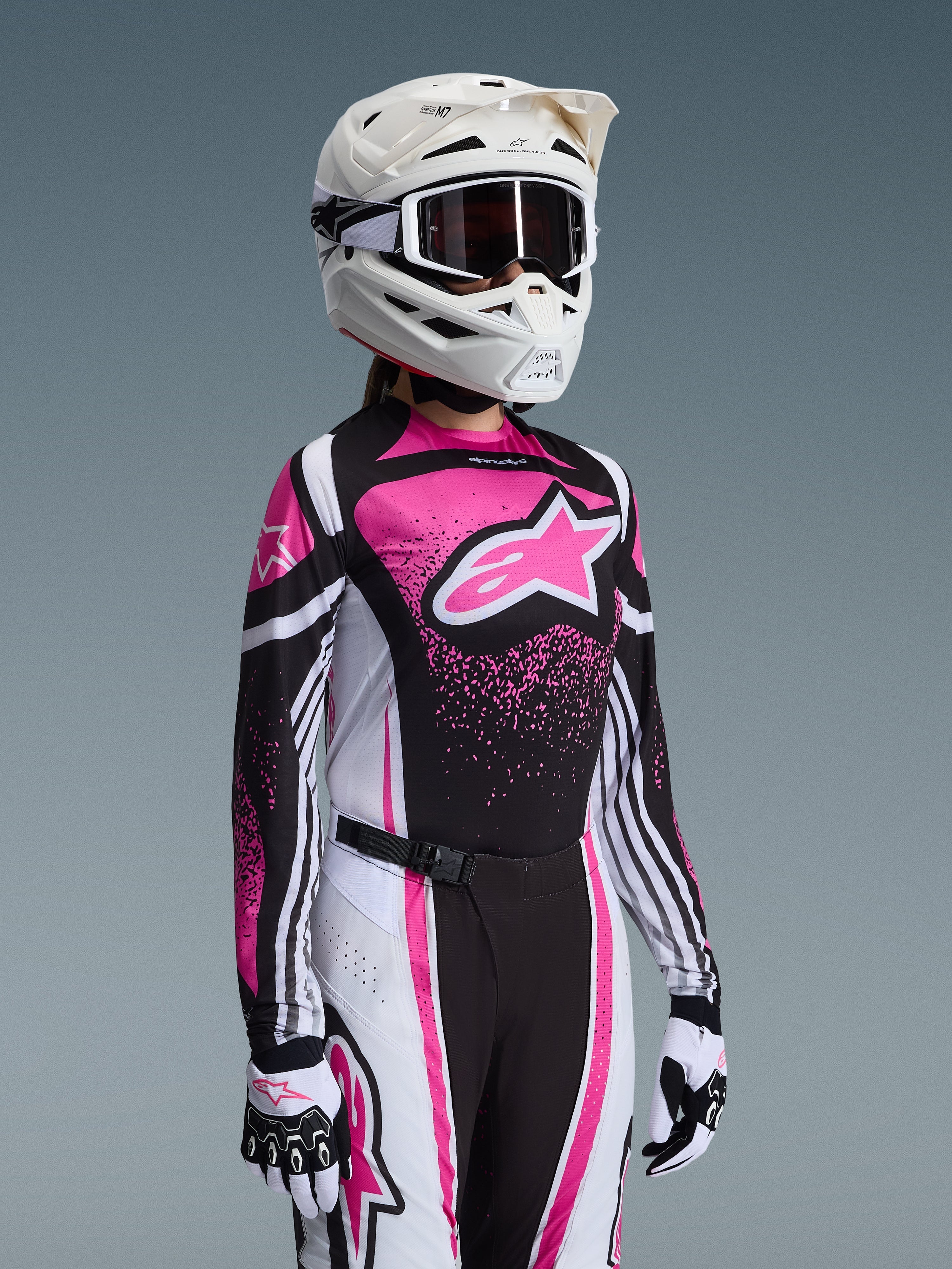 Motocross-Fahrerin im Alpinestars 2026 Stella Techstar Nomur Gear Set in Pink, Schwarz und Weiß; Trikot mit großem pinkfarbenem Stern-Logo, passende Hose mit Magnetschnalle, weißer Helm mit Goggles und weiß-schwarze Handschuhe.