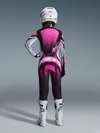 Alpinestars 2026 Stella Techstar Nomur Gear Set, Motocross-Fahrerin in der Rückansicht, pinkfarbenes und schwarzes Jersey mit weiß gestreiften Ärmeln und Sprenkelmuster, passende Hose mit weißem Alpinestars-Logo, weißer Helm und weiße Offroad-Stiefel