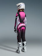 Motocross-Fahrerin von hinten im Alpinestars 2026 Stella Techstar Nomur Gear Set, Trikot und Hose in Schwarz und Pink mit weißen grafischen Akzenten, weißer Helm, weiß-schwarze Stiefel, professionell abgestimmte Rennausrüstung für Damen