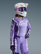 Alpinestars 2026 Damen Stella Fluid Apex Gear Set, lila und lavendelfarbenes Motocross-Trikot und Hose, getragen von einer Fahrerin mit weißem Helm und lila Goggles, mit markantem weißem Alpinestars-Branding und Logos