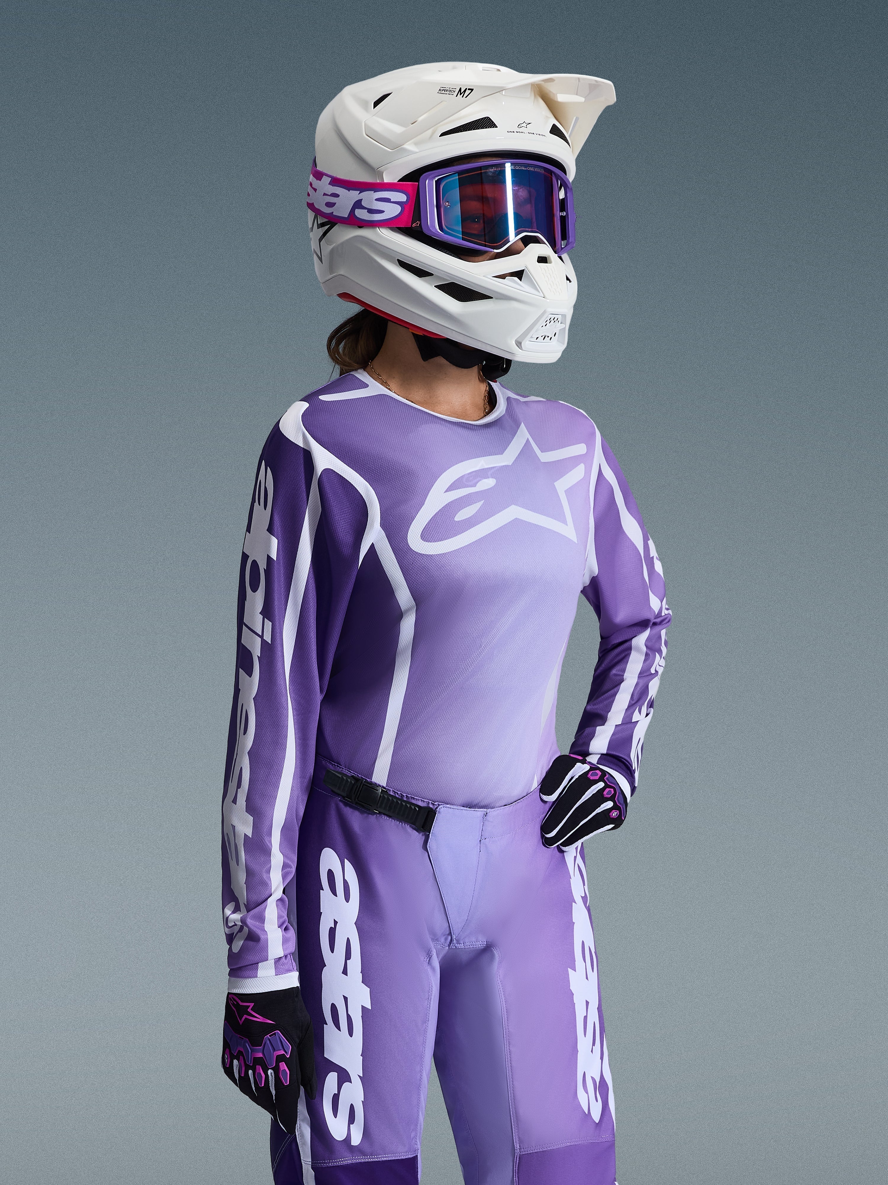 Alpinestars 2026 Damen Stella Fluid Apex Gear Set, lila und lavendelfarbenes Motocross-Trikot und Hose, getragen von einer Fahrerin mit weißem Helm und lila Goggles, mit markantem weißem Alpinestars-Branding und Logos