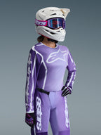 Motocross-Fahrerin im Alpinestars 2026 Stella Fluid Apex Bekleidungsset für Damen, lila-weißes Trikot mit Alpinestars-Logos, passende lila Hose, weißer Helm mit lila Brille und schwarz-lila Handschuhe, professionelle Offroad-Rennausrüstung