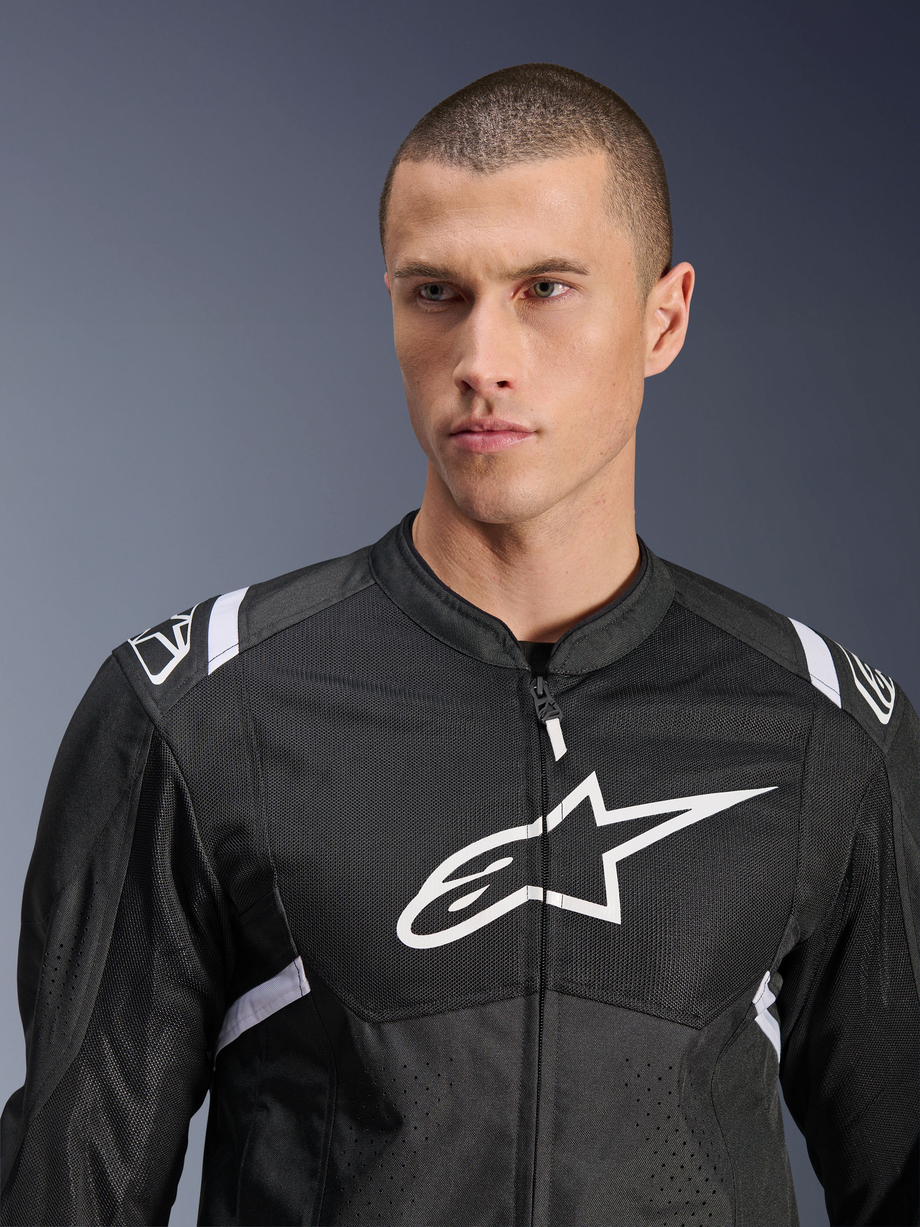 Alpinestars T-SPS Air V2 Jacke, Textil-Motorradjacke, Schwarz und Weiß mit großem weißem Brustlogo und Mesh-Einsätzen, sportliche Performance-Passform, getragen von männlichem Model