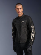 Alpinestars T-Dyno Air Jacket in Black, male model wearing a vintage-inspired textile motorcycle jacket with mesh panels for ventilation, large white Alpinestars logo on sleeves, paired with black riding gloves, urban motorcycle gear design